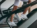 Kobieta w białych spodenkach i butach sportowych wchodzi po schodach na bieżni. To świetny trening cardio, który wzmacnia nogi i poprawia kondycję.