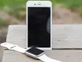 Biały smartwatch i telefon leżą na drewnianym blacie. Dowiedz się, jak zainstalować smartwatch, by połączyć go z telefonem.