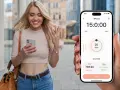 Uśmiechnięta kobieta z telefonem zastanawia się, dlaczego smartwatch nie liczy kroków. Na ekranie telefonu widać aplikację z danymi o aktywności.