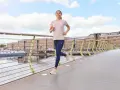 Uśmiechnięta kobieta w sportowym stroju biegnie po moście. Widać jej zadowolenie z efektów biegania.
