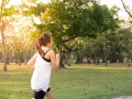 Kobieta w sportowym stroju biegnie przez park. Słońce przebija się przez drzewa, tworząc ciepłą atmosferę. To idealny dzień na realizację jej marszobieg planu.