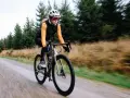 Kobieta na rowerze gravelowym jedzie po szutrowej drodze, co od razu pokazuje, czym się różni gravel od szosy.