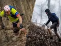 Dwóch biegaczy pokonuje trudny teren podczas Barkley Marathon. Jeden wspina się po drzewach, drugi używa kijków.
