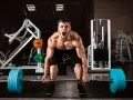 Mężczyzna z maksymalnym wysiłkiem podnosi sztangę, krzycząc z bólu i determinacji. Jego twarz wyraża 10 w skali Borga.