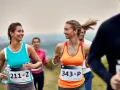 Uśmiechnięte biegaczki na polskim półmaratonie. Dwie kobiety w sportowych strojach biegną, jedna trzyma butelkę wody.