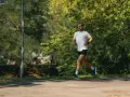 Mężczyzna w białej koszulce i czarnych spodenkach biegnie po ścieżce w parku. To jego półmaraton czas amatora, trening przed ważnym biegiem.