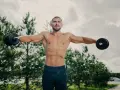 Mężczyzna ćwiczy na świeżym powietrzu, wykonując boczne unoszenie ramion z hantlami. To świetny sposób, jak poszerzyć barki i zbudować sylwetkę.