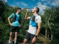 Dwóch biegaczy w kamizelkach nawadniających, jeden pije wodę. Klucz do tego, jak przygotować się do maratonu, to odpowiednie nawodnienie i trening.
