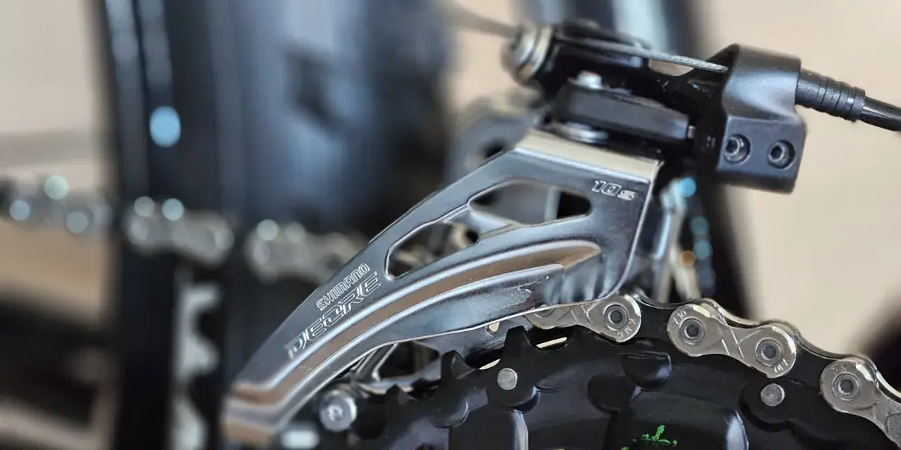 Precyzyjna regulacja przerzutek w rowerze Shimano Deore. Widoczny mechanizm przerzutki przedniej i fragment łańcucha.