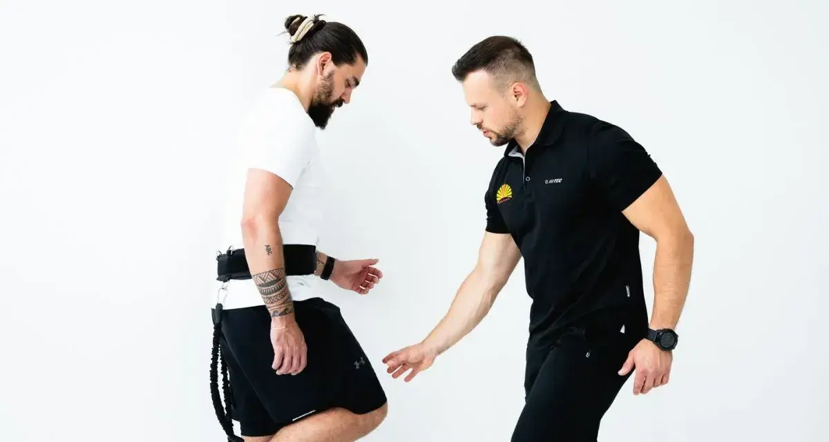 Trener koryguje technikę biegu u mężczyzny z pasem i linkami.