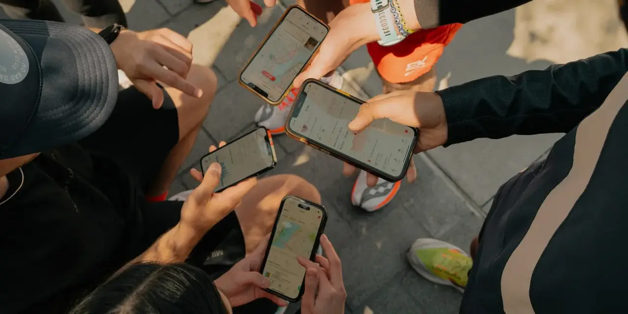 Grupa biegaczy analizuje swoje wyniki na telefonach. Widać mapy tras i statystyki aktywności, typowe dla aplikacji Strava po polsku.