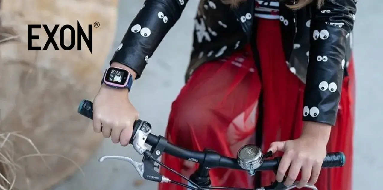 Dziecko w kurtce z oczkami trzyma kierownicę roweru. Na ręce ma różowy pasek do smartwatch dla dzieci.