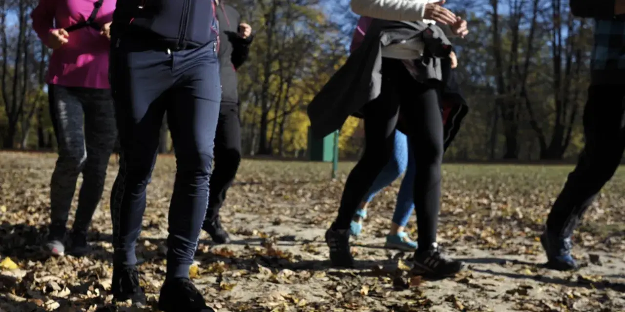 Grupa osób uprawia slow jogging w parku jesienią. Widać ich nogi i fragmenty ubrań. To świetne efekty dla zdrowia i samopoczucia.