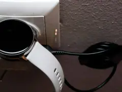 Biały smartwatch z czarnym ekranem podłączony do ładowarki w gniazdku. Prosty sposób, jak ładować smartwatch, by był gotowy do użycia.