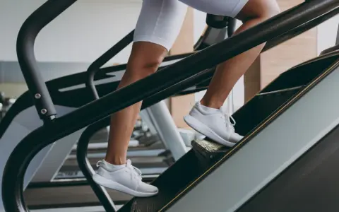 Kobieta w białych spodenkach i butach sportowych wchodzi po schodach na bieżni. To świetny trening cardio, który wzmacnia nogi i poprawia kondycję.