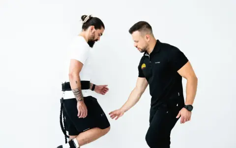 Trener koryguje technikę biegu u mężczyzny z pasem i linkami.