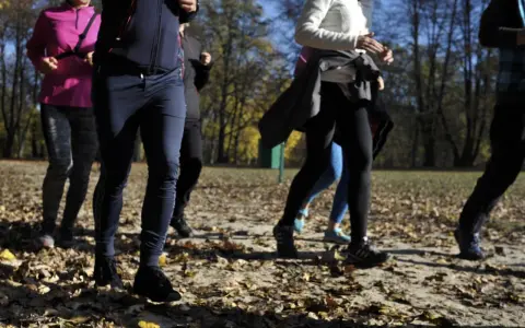 Grupa osób uprawia slow jogging w parku jesienią. Widać ich nogi i fragmenty ubrań. To świetne efekty dla zdrowia i samopoczucia.