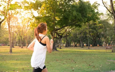 Kobieta w sportowym stroju biegnie przez park. Słońce przebija się przez drzewa, tworząc ciepłą atmosferę. To idealny dzień na realizację jej marszobieg planu.