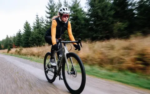 Kobieta na rowerze gravelowym jedzie po szutrowej drodze, co od razu pokazuje, czym się różni gravel od szosy.