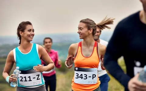Uśmiechnięte biegaczki na polskim półmaratonie. Dwie kobiety w sportowych strojach biegną, jedna trzyma butelkę wody.