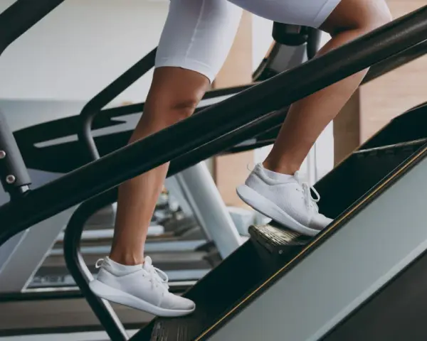 Kobieta w białych spodenkach i butach sportowych wchodzi po schodach na bieżni. To świetny trening cardio, który wzmacnia nogi i poprawia kondycję.