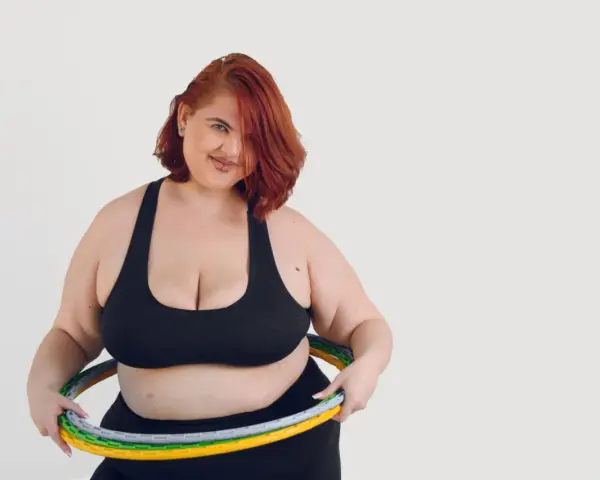 Kobieta z rudymi włosami i hula hop z obciążeniem. Dowiedz się, jak kręcić hula hop z obciążeniem, aby wzmocnić mięśnie brzucha.