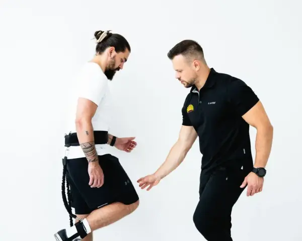 Trener koryguje technikę biegu u mężczyzny z pasem i linkami.