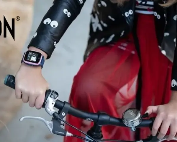 Dziecko w kurtce z oczkami trzyma kierownicę roweru. Na ręce ma różowy pasek do smartwatch dla dzieci.