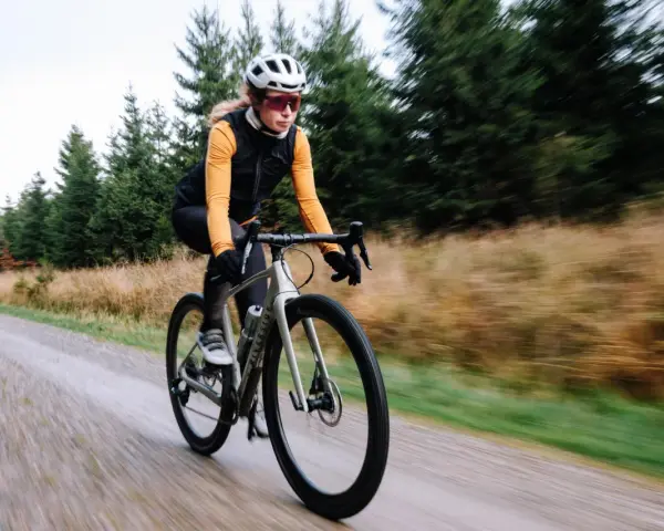 Kobieta na rowerze gravelowym jedzie po szutrowej drodze, co od razu pokazuje, czym się różni gravel od szosy.