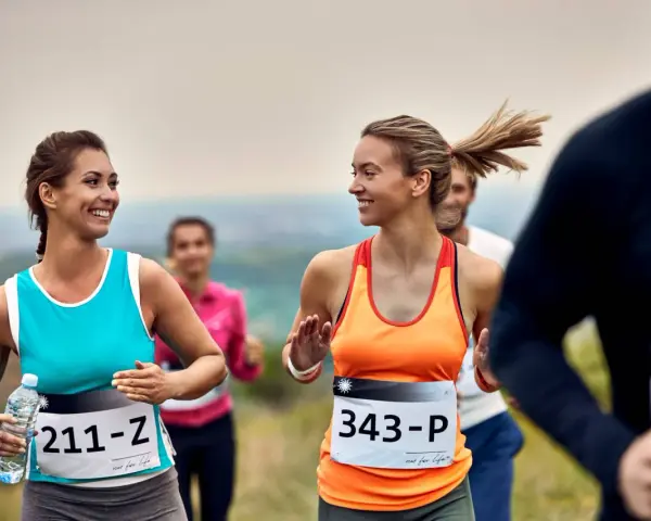 Uśmiechnięte biegaczki na polskim półmaratonie. Dwie kobiety w sportowych strojach biegną, jedna trzyma butelkę wody.