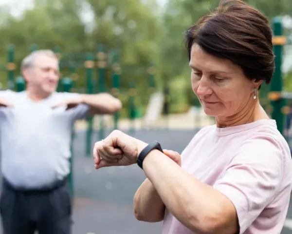 Kobieta sprawdza na zegarku dane treningowe, być może porównując je z tabelą długość kroku człowieka.