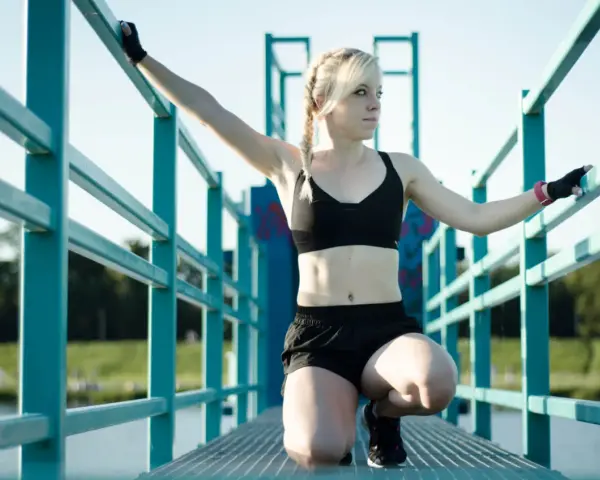 Kobieta w stroju sportowym, z rękami opartymi o turkusową balustradę, może odczuwać lekkie złe samopoczucie po wysiłku fizycznym.