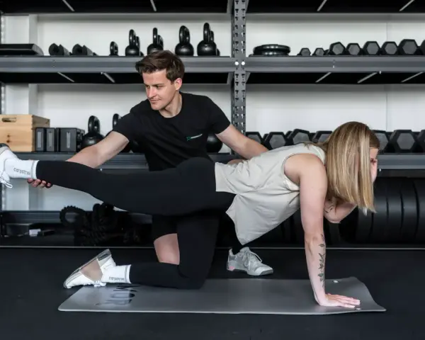Trener pomaga kobiecie w ćwiczeniu, które zapobiega zakwasom po treningu.