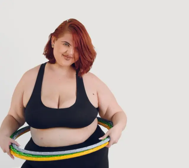 Kobieta z rudymi włosami i hula hop z obciążeniem. Dowiedz się, jak kręcić hula hop z obciążeniem, aby wzmocnić mięśnie brzucha.