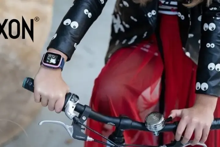 Dziecko w kurtce z oczkami trzyma kierownicę roweru. Na ręce ma różowy pasek do smartwatch dla dzieci.