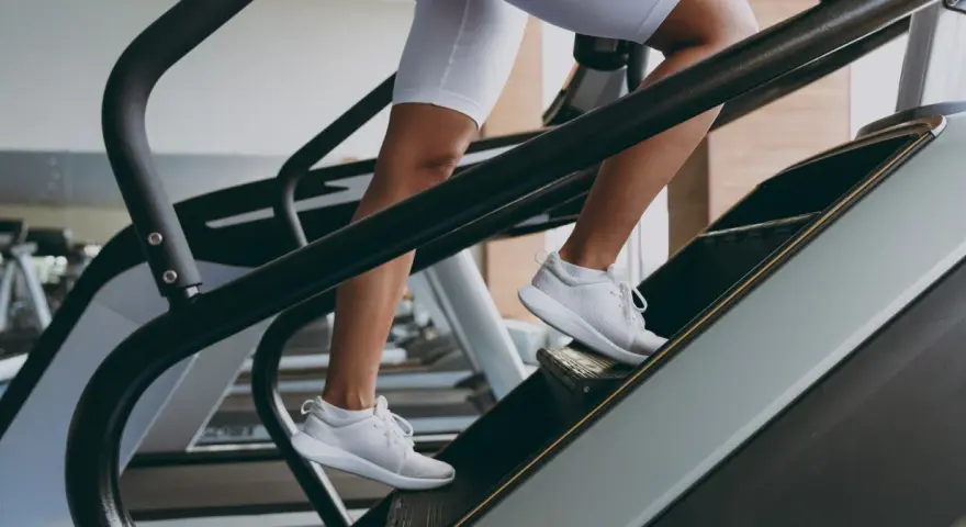 Kobieta w białych spodenkach i butach sportowych wchodzi po schodach na bieżni. To świetny trening cardio, który wzmacnia nogi i poprawia kondycję.
