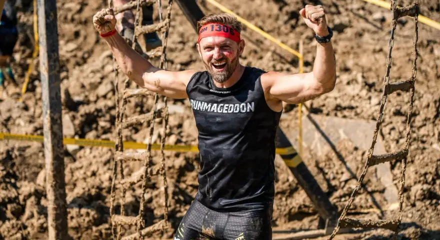 Szczęśliwy uczestnik Runmageddonu z podniesionymi pięściami, ubrany w koszulkę z napisem "RUNMageddon".