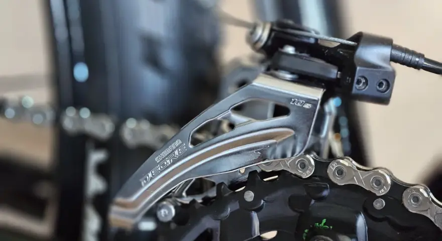 Precyzyjna regulacja przerzutek w rowerze Shimano Deore. Widoczny mechanizm przerzutki przedniej i fragment łańcucha.