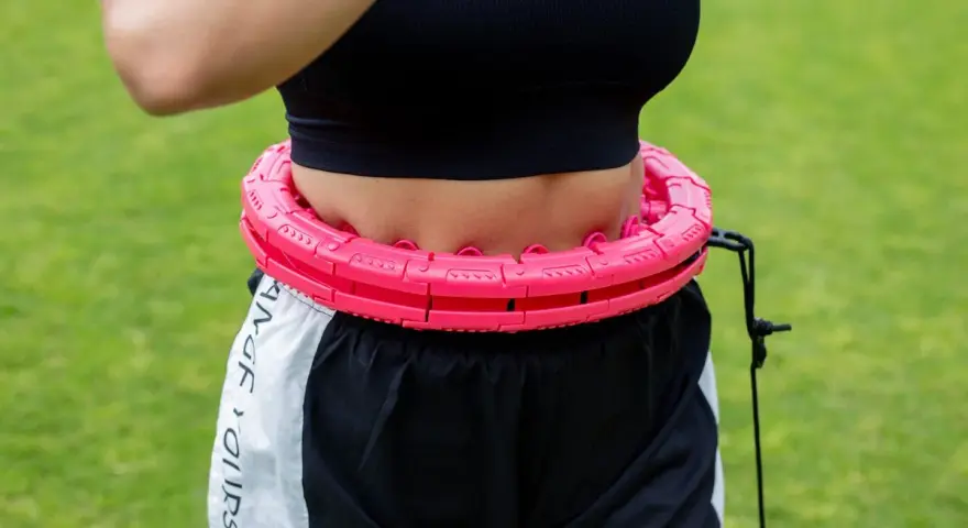 Kobieta ćwiczy z różowym hula hop. Czy hula hop jest szkodliwe? Ten model wydaje się bezpieczny i skuteczny.