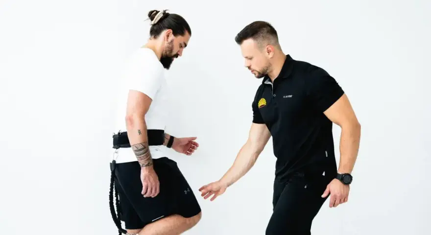 Trener koryguje technikę biegu u mężczyzny z pasem i linkami.