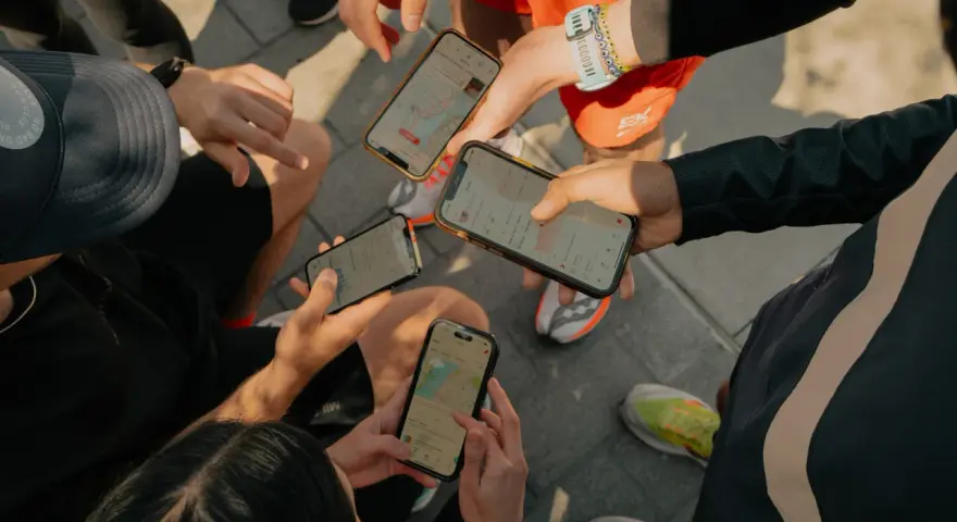 Grupa biegaczy analizuje swoje wyniki na telefonach. Widać mapy tras i statystyki aktywności, typowe dla aplikacji Strava po polsku.