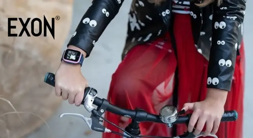 Dziecko w kurtce z oczkami trzyma kierownicę roweru. Na ręce ma różowy pasek do smartwatch dla dzieci.