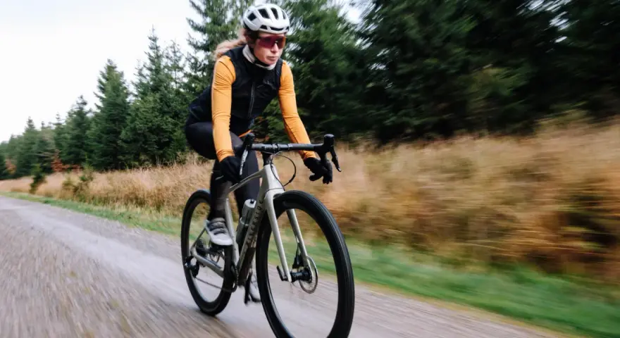 Kobieta na rowerze gravelowym jedzie po szutrowej drodze, co od razu pokazuje, czym się różni gravel od szosy.