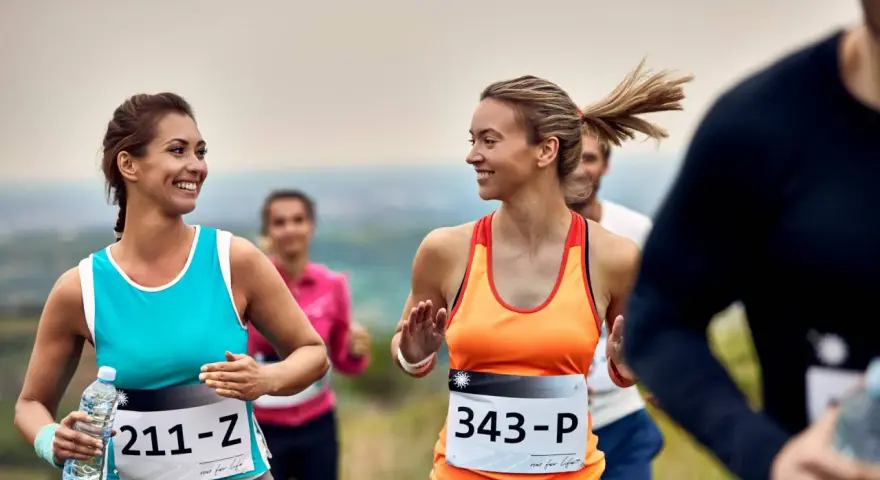 Uśmiechnięte biegaczki na polskim półmaratonie. Dwie kobiety w sportowych strojach biegną, jedna trzyma butelkę wody.