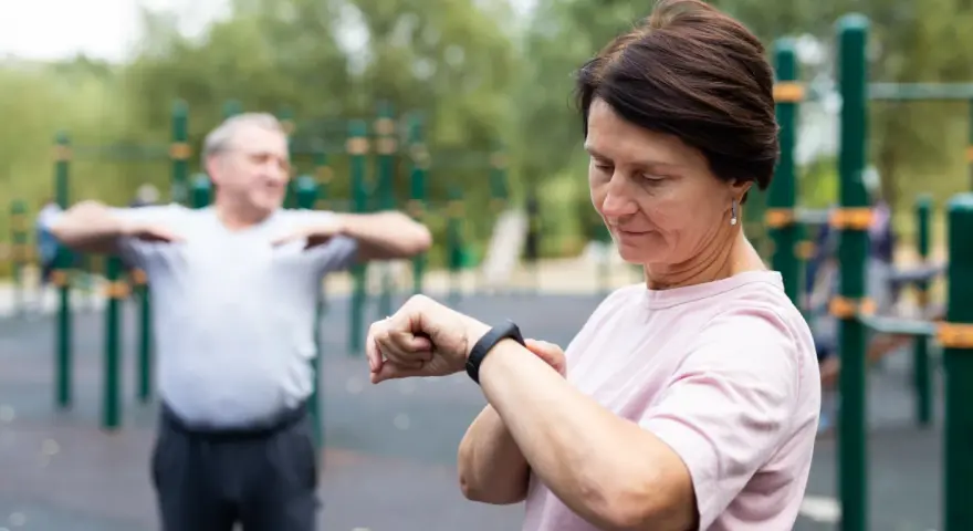 Kobieta sprawdza na zegarku dane treningowe, być może porównując je z tabelą długość kroku człowieka.