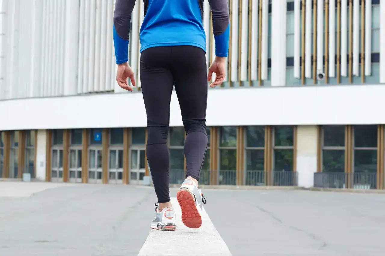 Spacer 3 km ile kalorii spala? Mężczyzna w sportowym stroju idzie po murku przed nowoczesnym budynkiem.