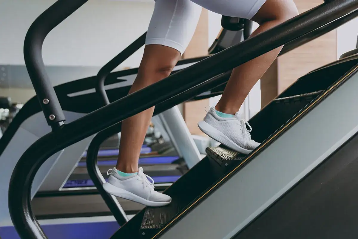 Kobieta w białych butach sportowych wchodzi po schodach. Wchodzenie po schodach to świetny trening cardio i wzmacniający nogi.