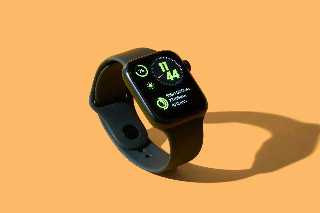 Czarny smartwatch na pomarańczowym tle. Ekran pokazuje godzinę 11:44, aktywność i kroki. Dowiedz się, jak ustawić krokomierz na rękę.