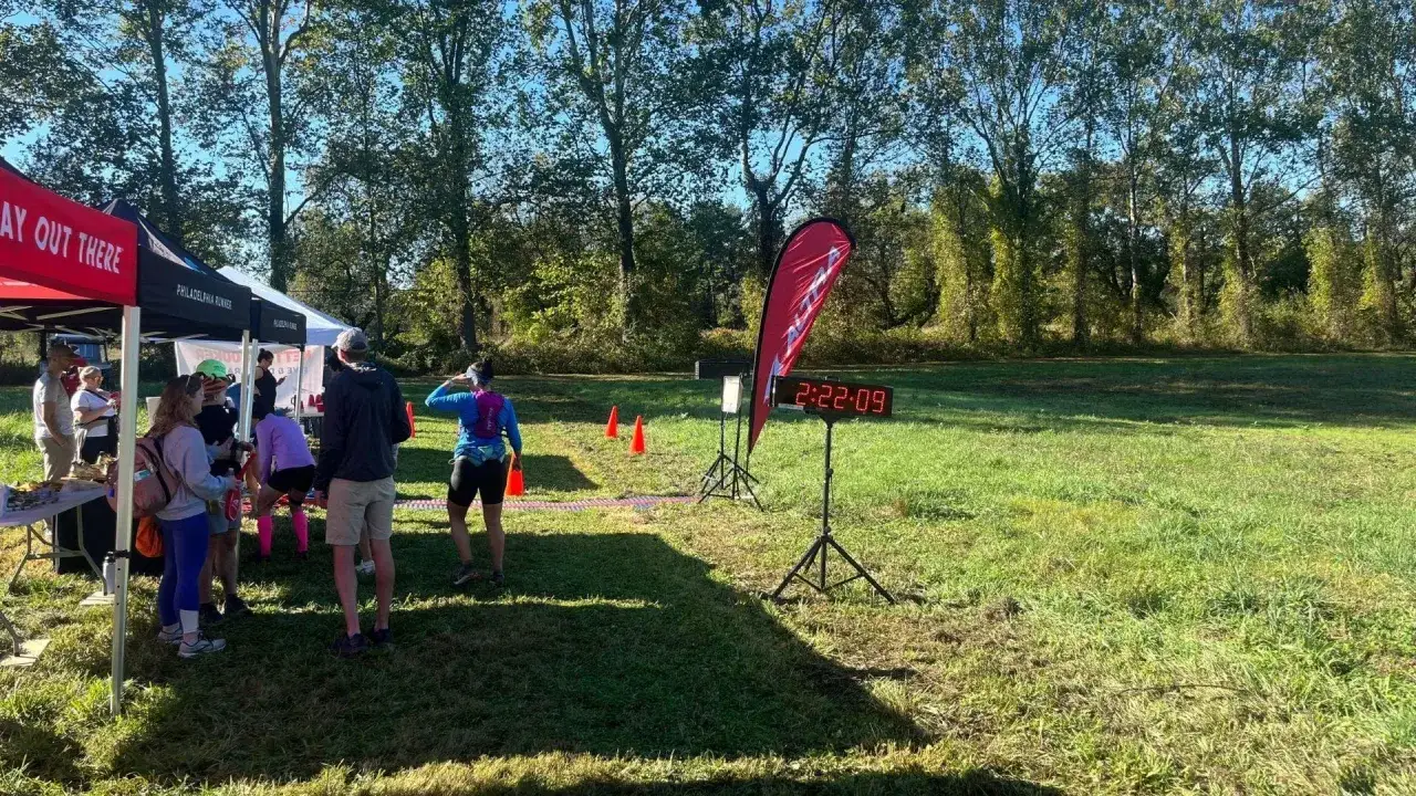 Zawodnicy czekają na start biegu na 10 km. Na pierwszym planie cyfrowy zegar pokazujący czas.