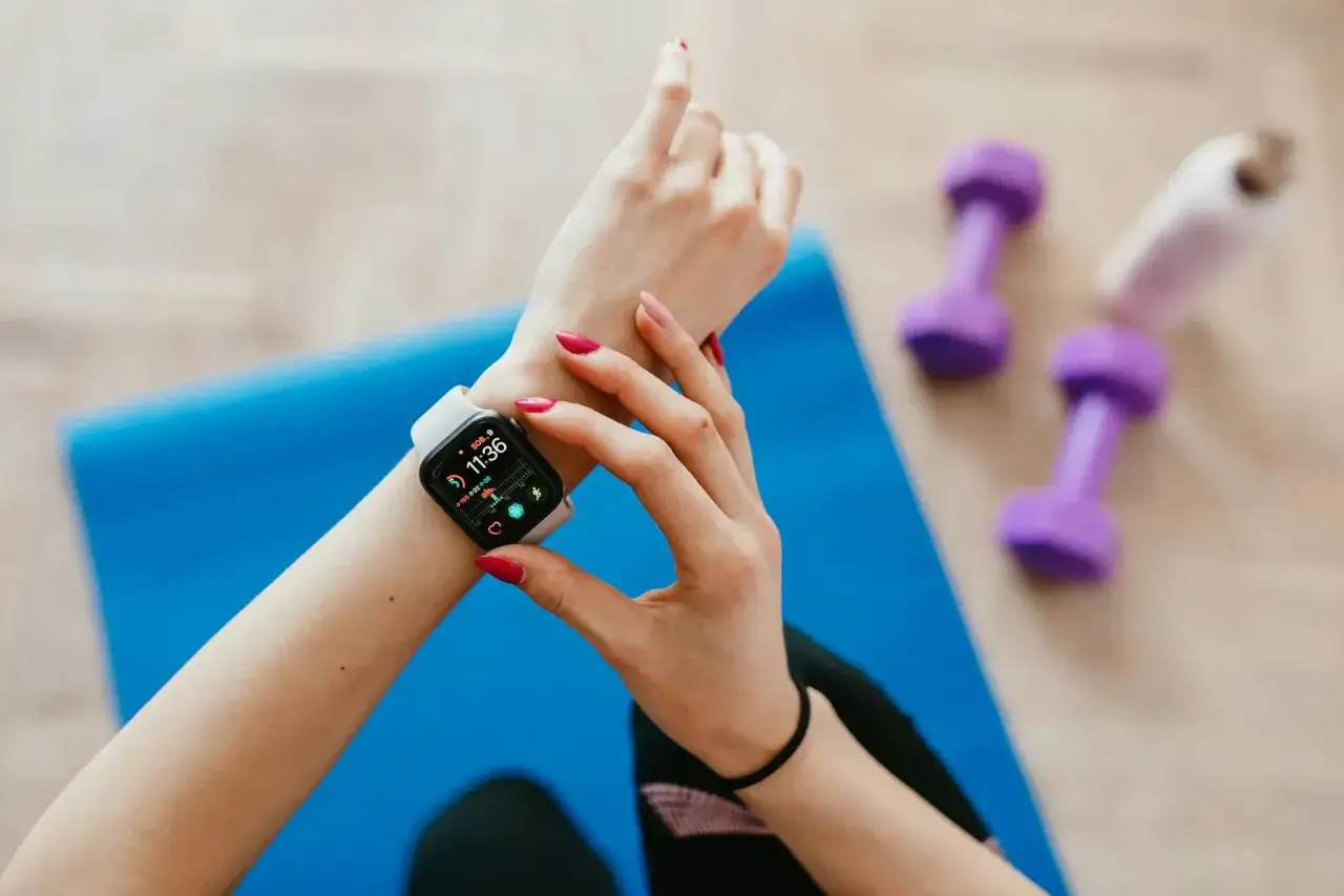 Kobieta sprawdza na swoim smartwatchu, co to jest smartwatch, dane treningowe. Obok leżą fioletowe hantle.